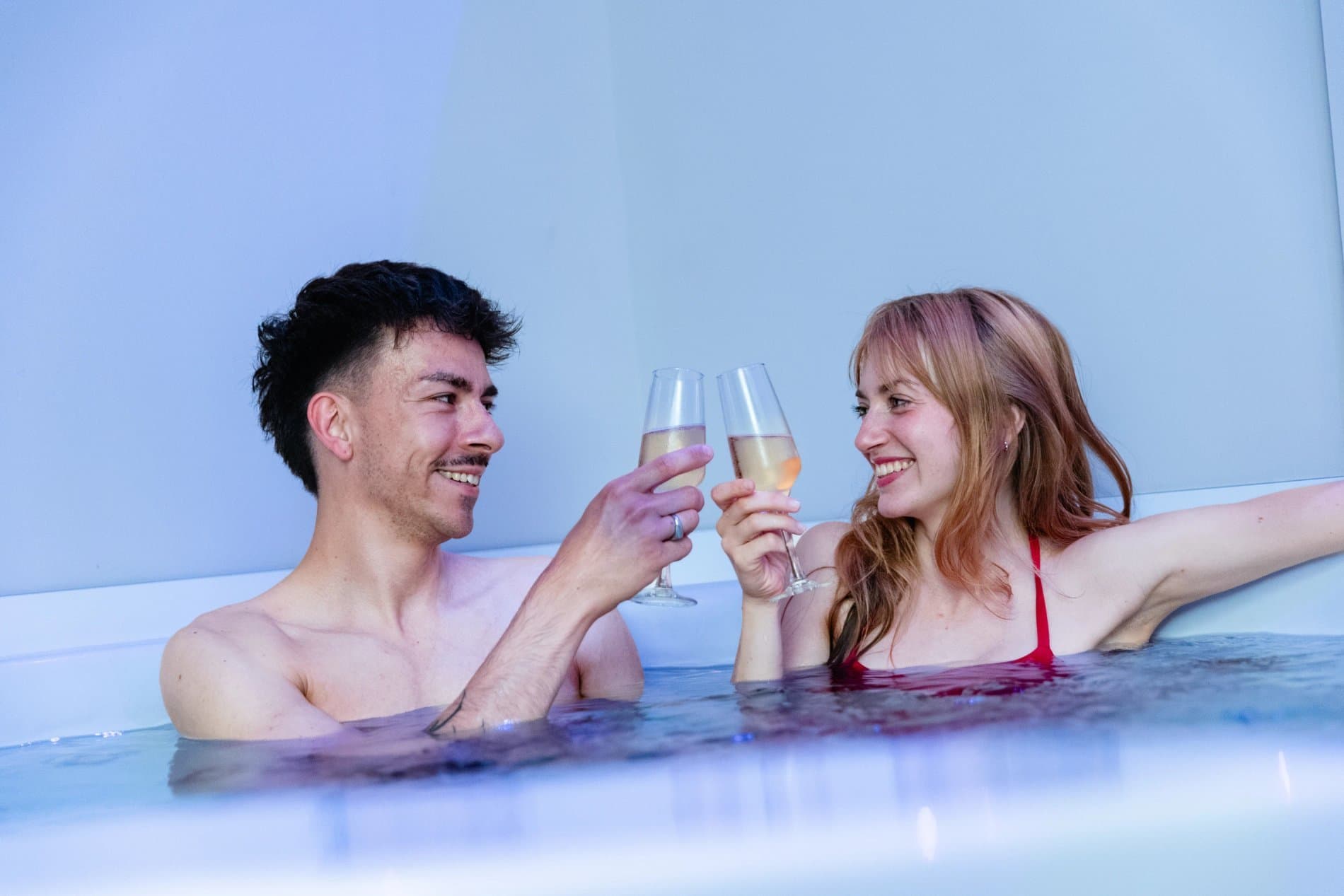 Couple toasting with champagne flutes while relaxing in indoor pool.