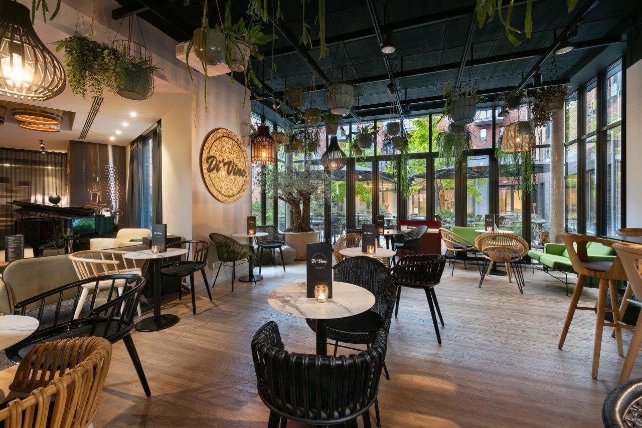Modern restaurant and lounge with hanging plants, floor-to-ceiling windows, contemporary furniture and natural lighting.