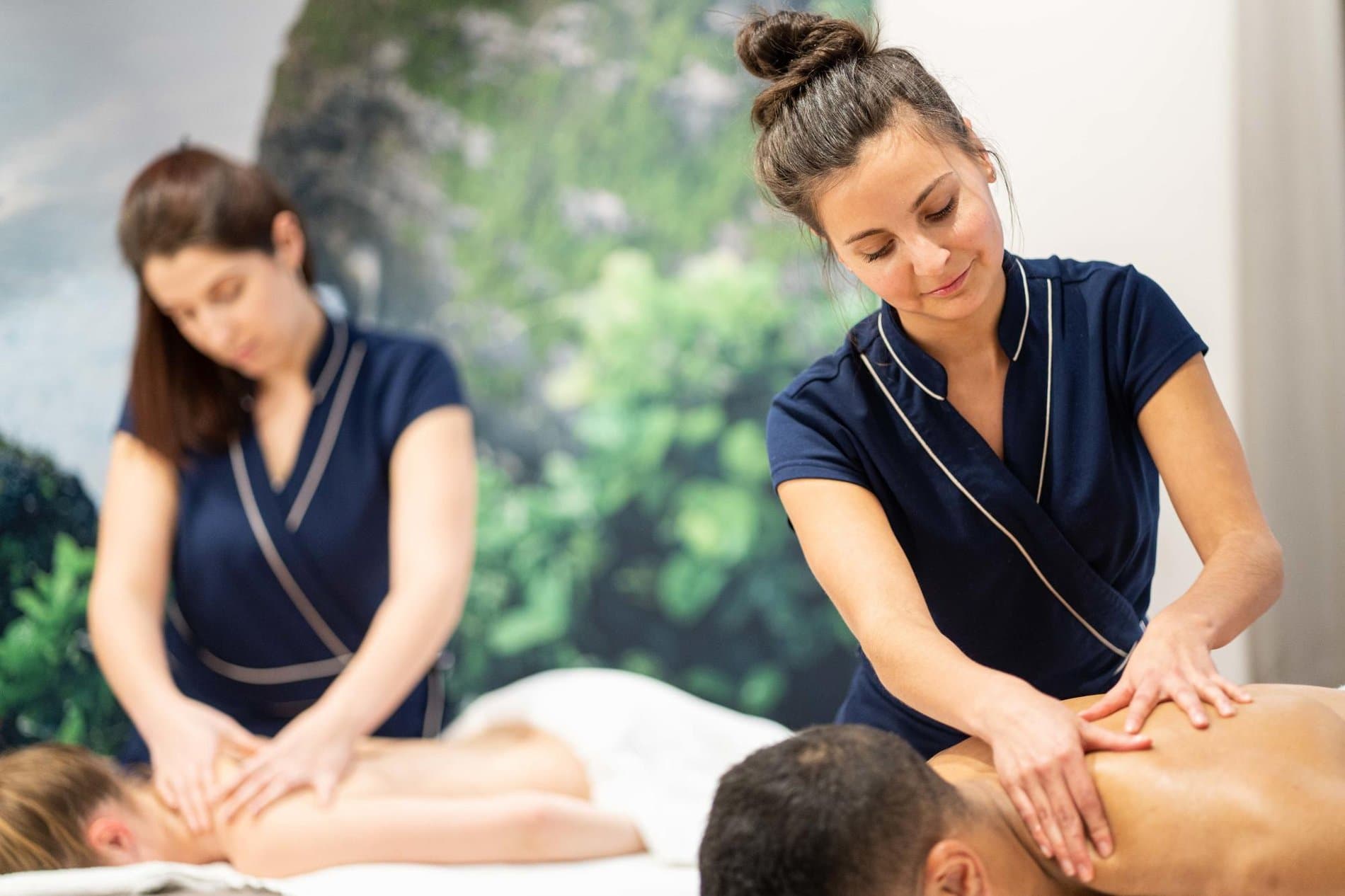 Professional spa therapists performing massage treatments on clients in relaxation room.