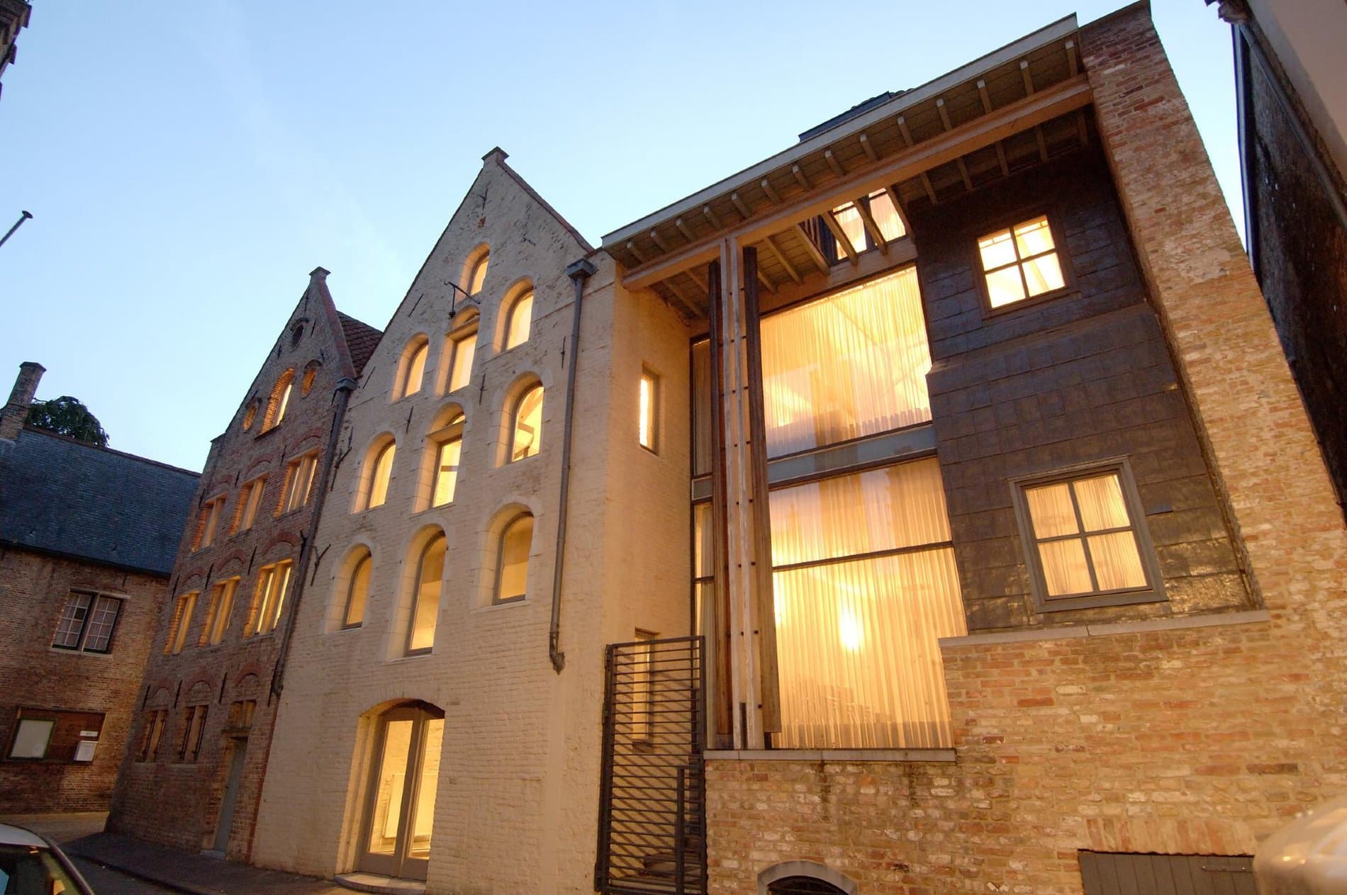 Illuminated brick facade of converted heritage building with modern glazed entrance extension at dusk.