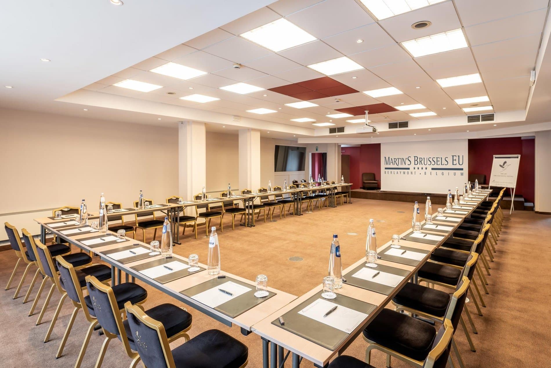 Professional conference room with long tables, water glasses, notepads setup ready.