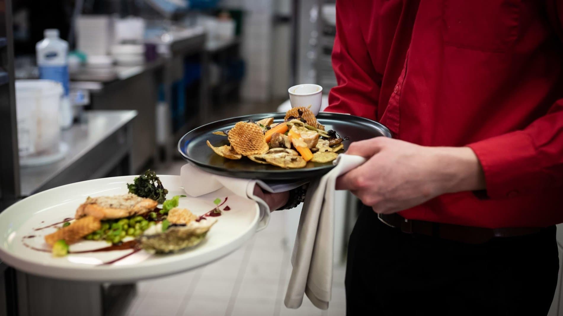 Chef in red shirt presenting plated dish and fried vegetable appetizer in kitchen.