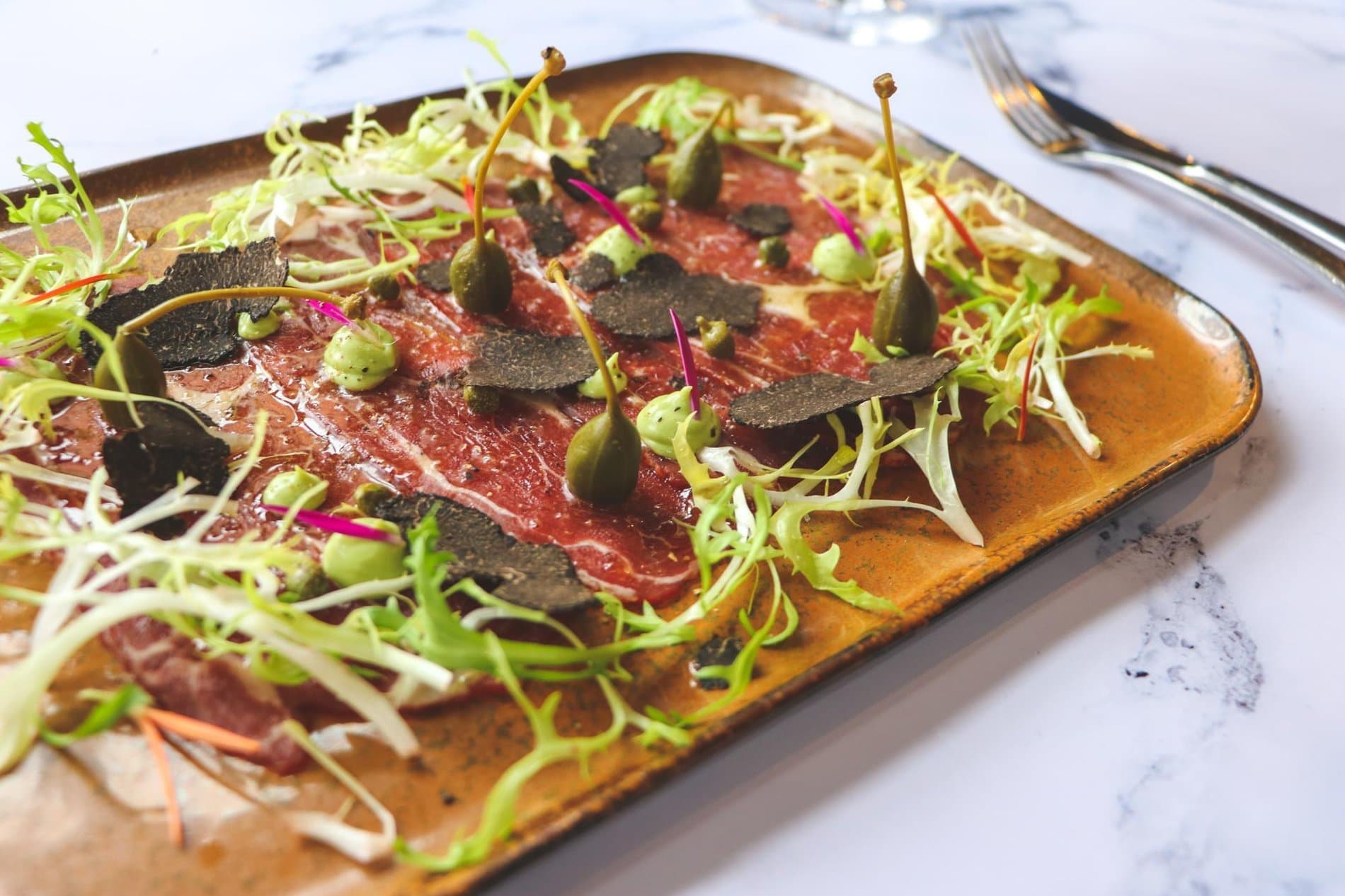 Artfully plated cured meat and microgreens on rustic wooden serving board.