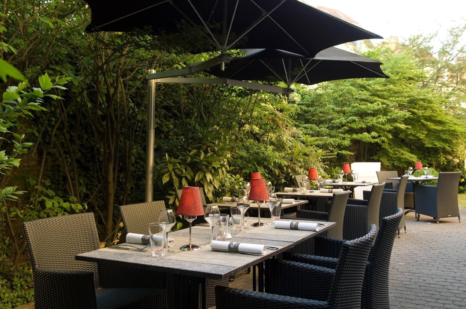 Outdoor dining terrace with black umbrellas, wicker chairs, and lush garden surroundings.
