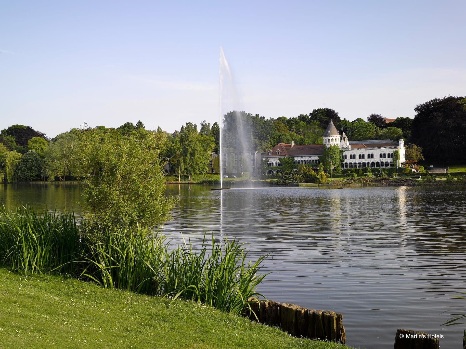 Lakeside manor grounds with fountain, manicured lawn, trees and water views.