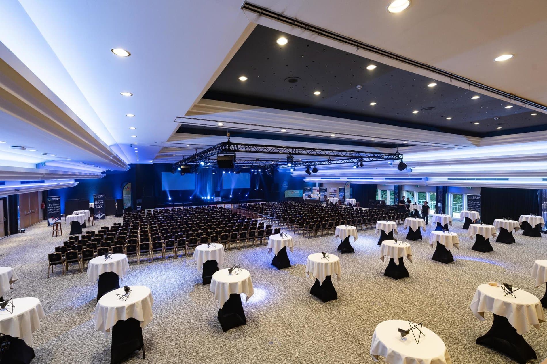 Large event space with banquet tables, stage lighting, and professional audio-visual setup ready.