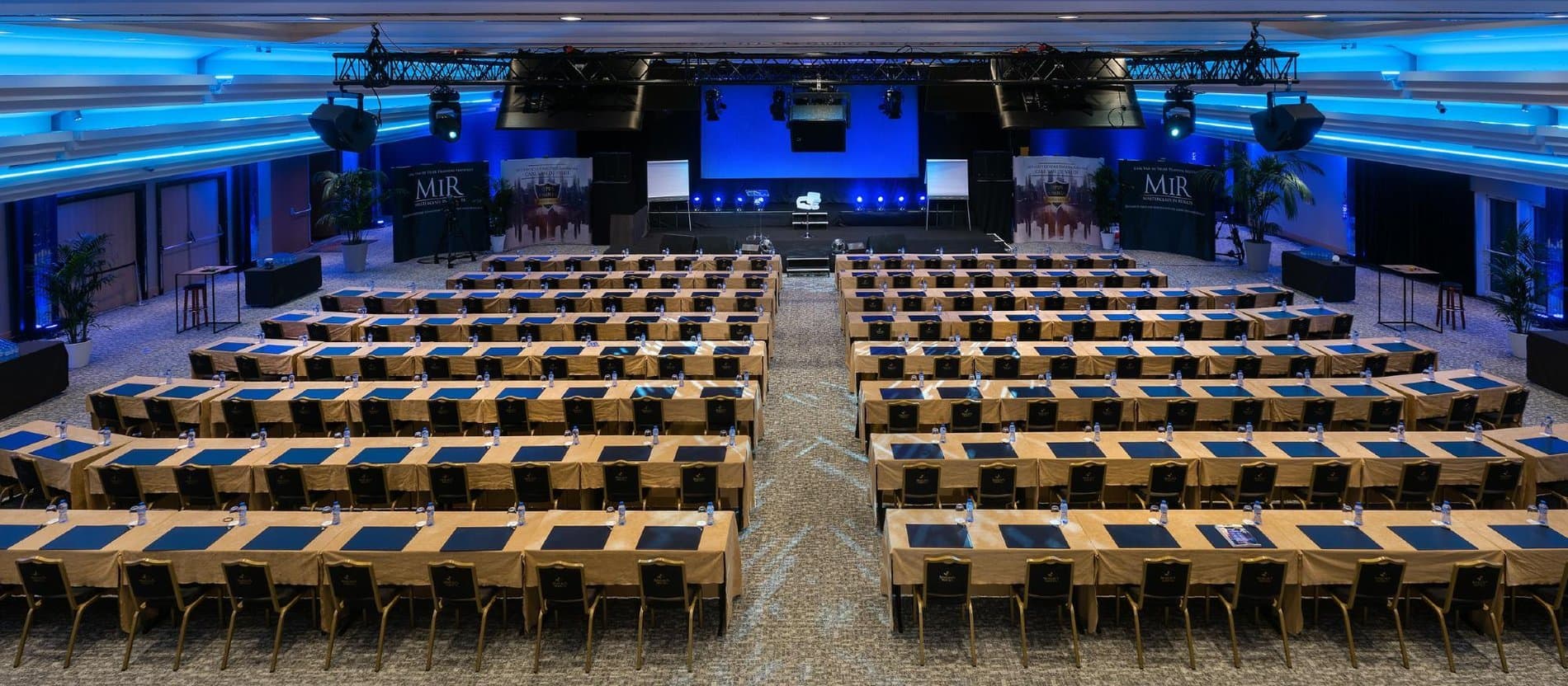 Large conference hall with theater-style seating, stage, and blue ambient lighting.
