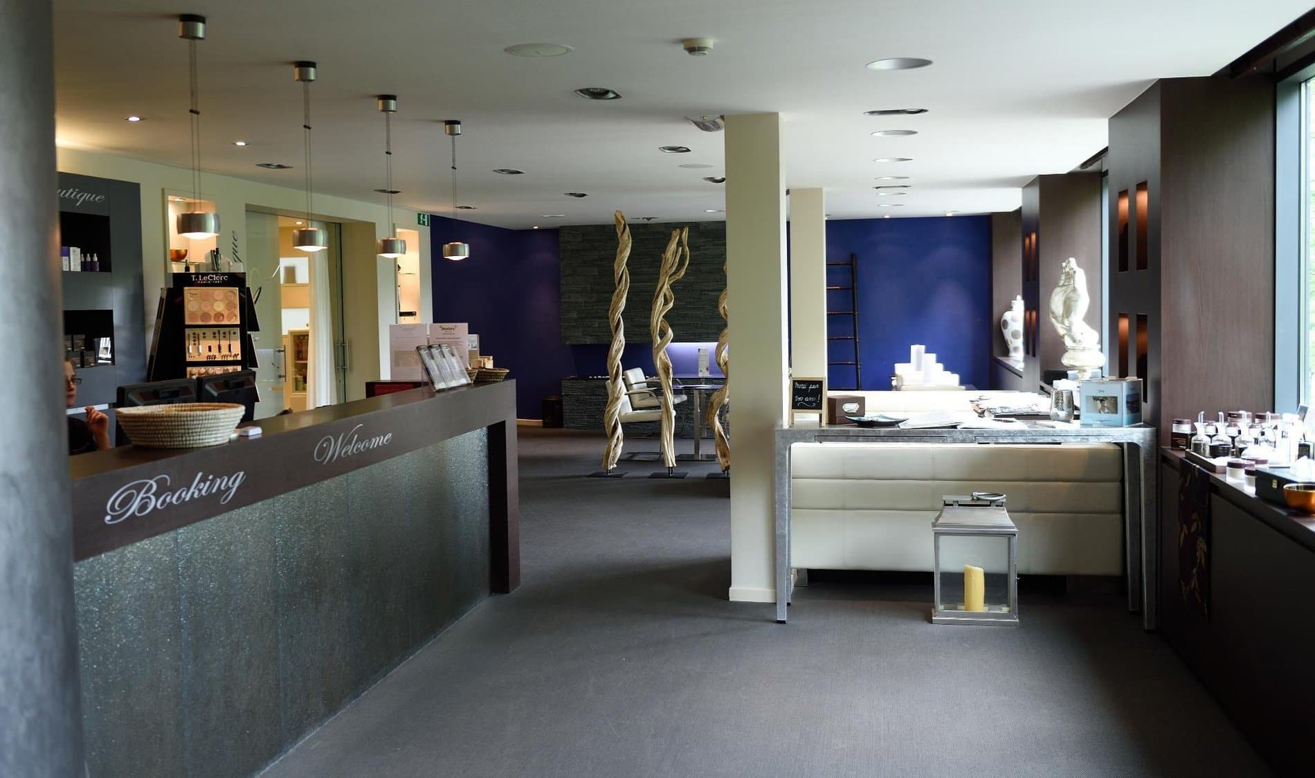 Upscale spa reception lobby with booking desk, retail display, and decorative sculptures.