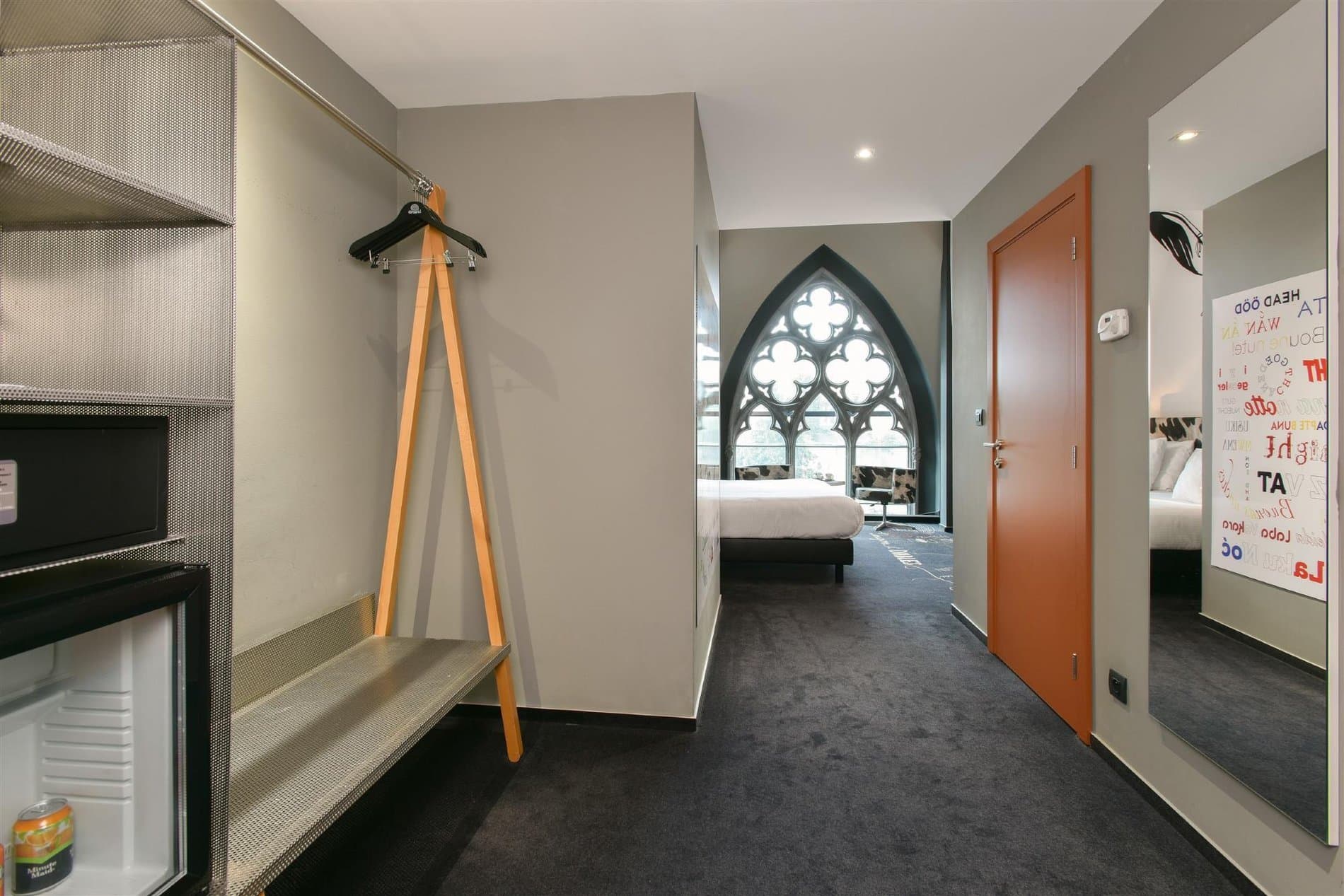 Modern hotel hallway with bedroom visible, geometric window, wooden coat stand detail.