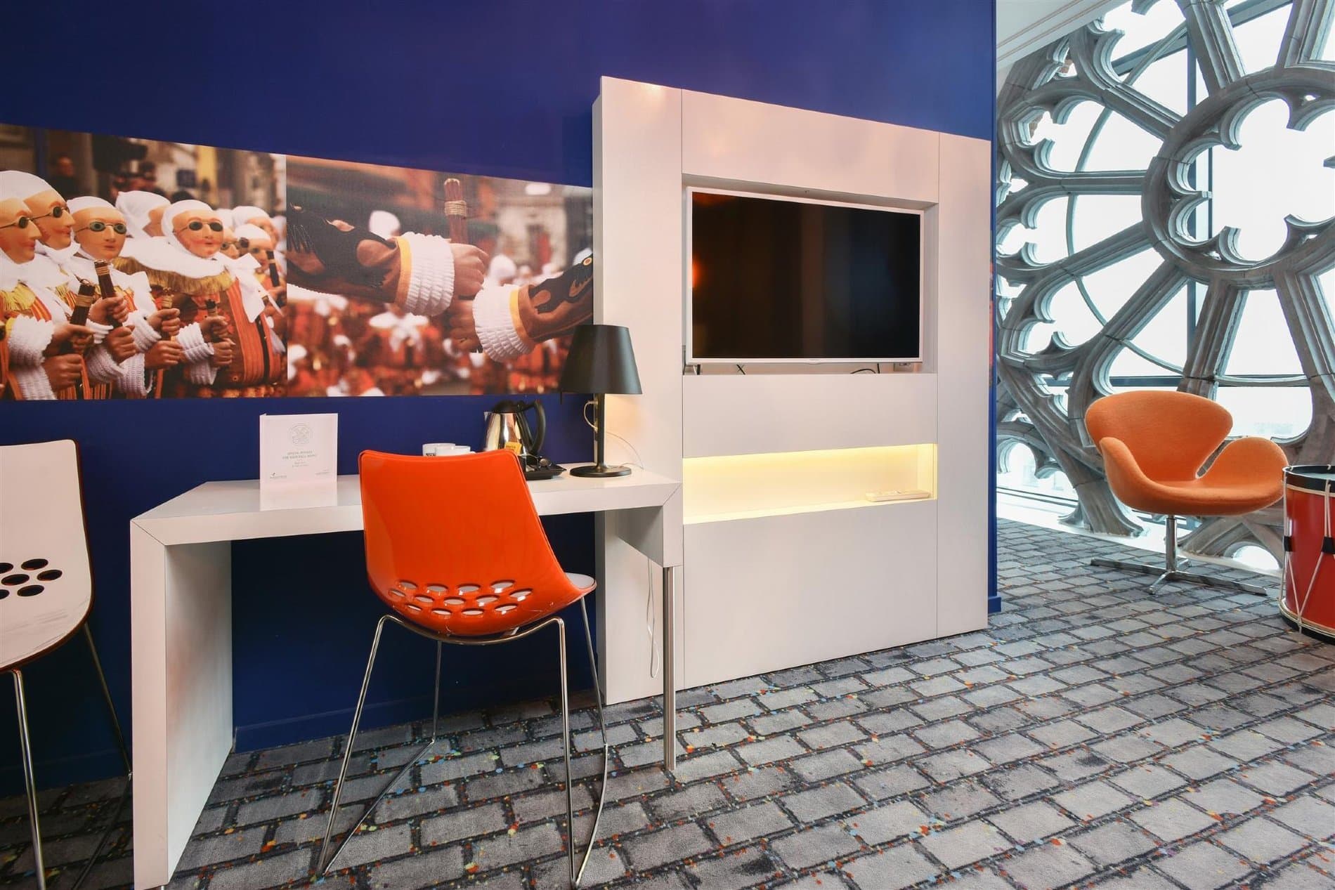 Modern reception desk with orange chair, artwork, and decorative architectural window detail.