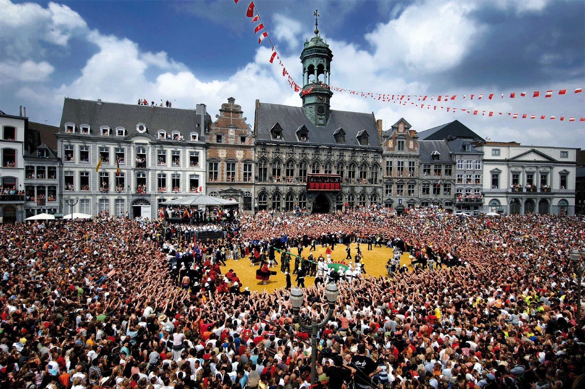 Large public square courtyard with historic European architecture and massive crowd gathering.