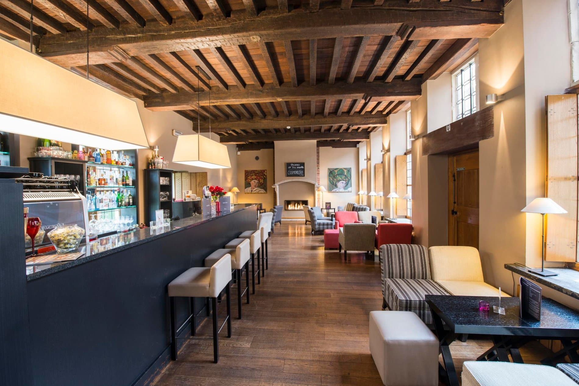 Upscale hotel lobby with bar, lounge seating, fireplace, and exposed wooden ceiling beams.