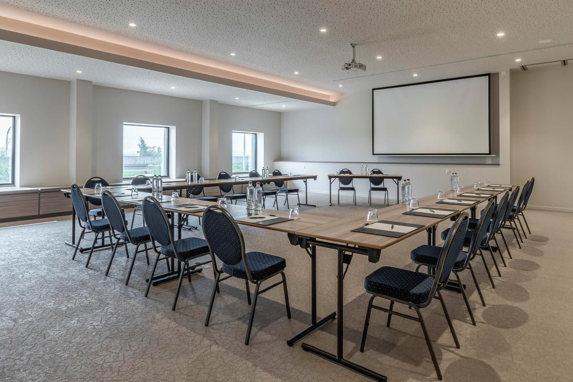 Modern conference room with projection screen, meeting tables, and natural light from windows.
