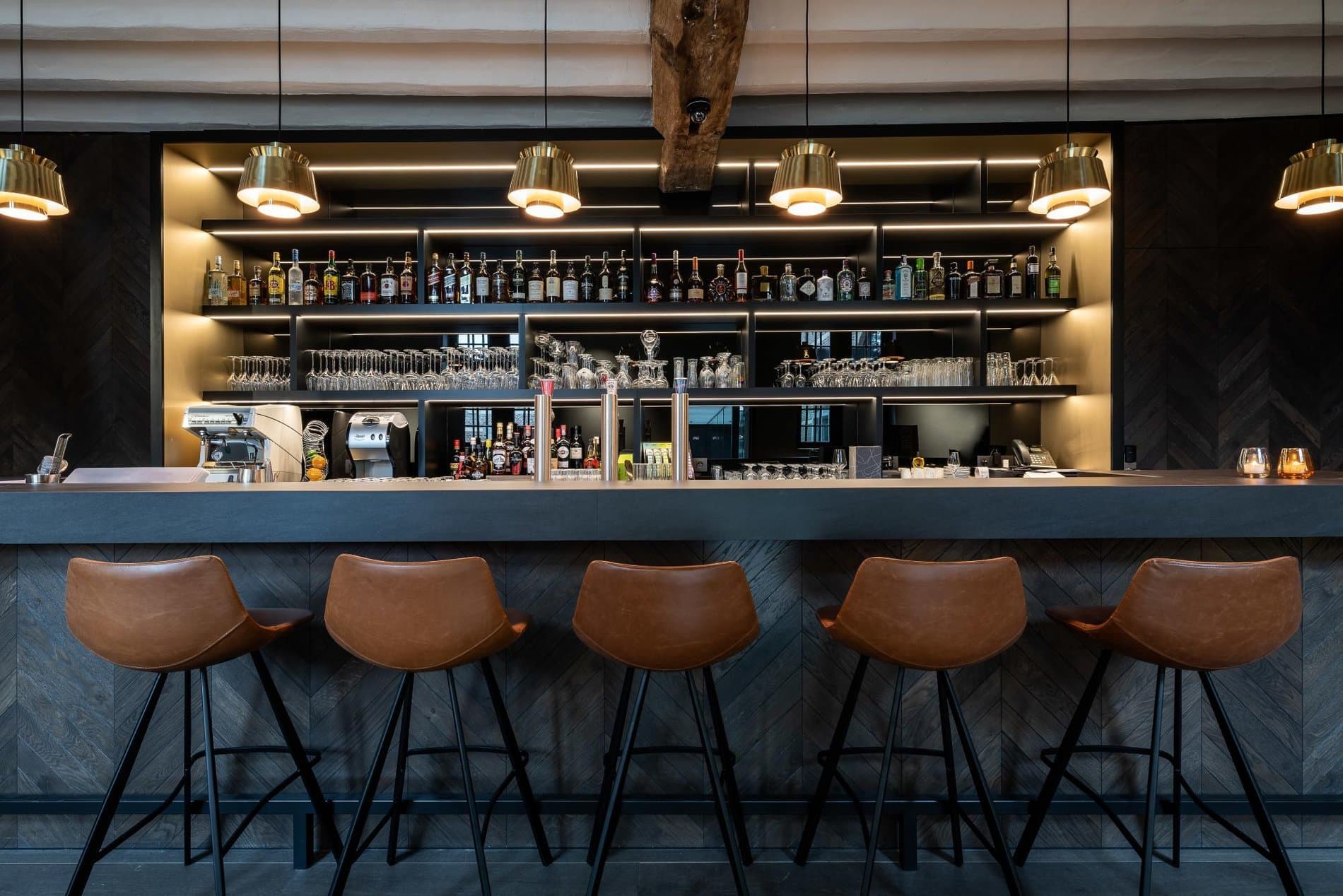 Modern hotel bar with leather stools, illuminated bottle display, and polished aesthetic.