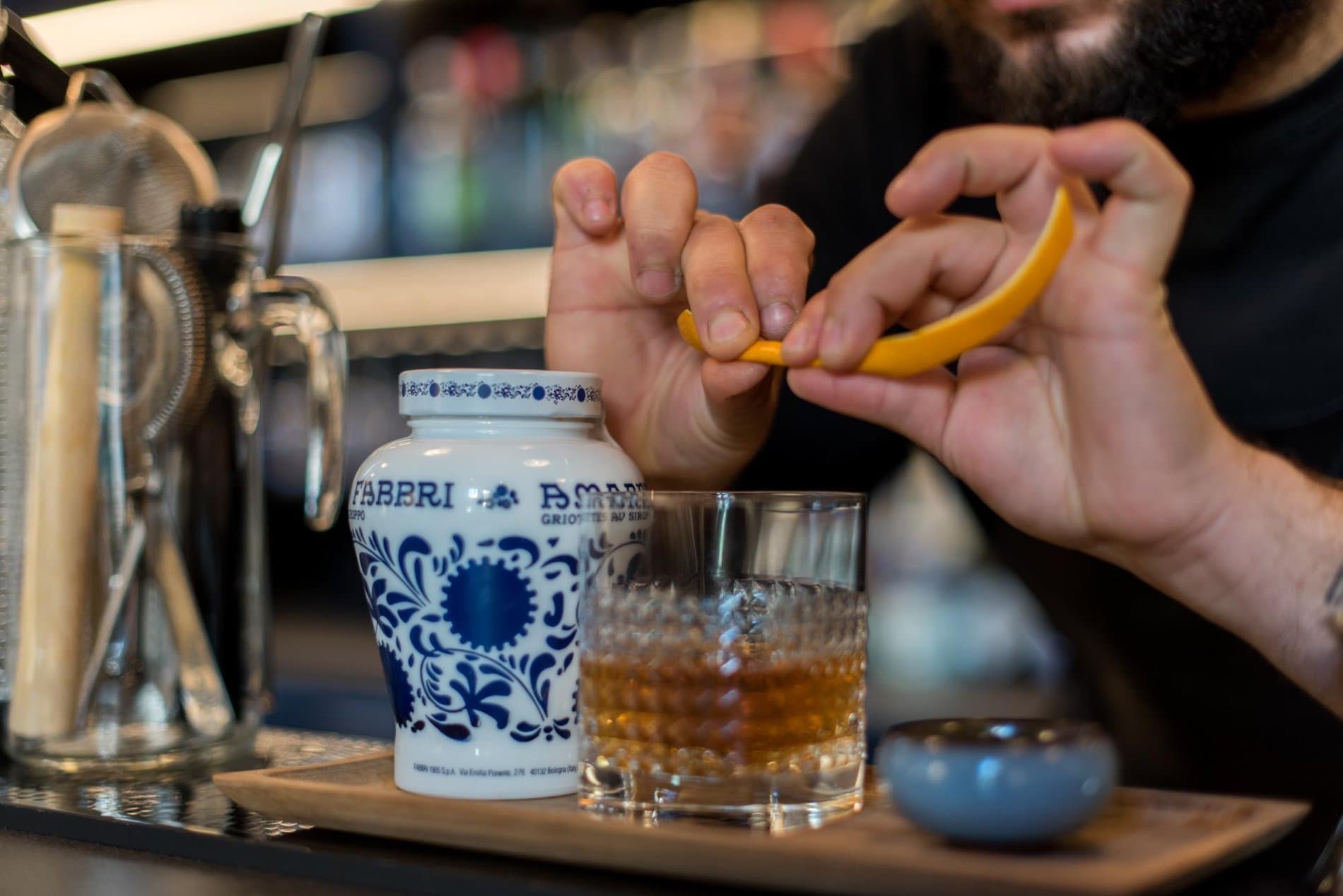 Hand squeezing lemon into a glass of amber spirit at bar counter