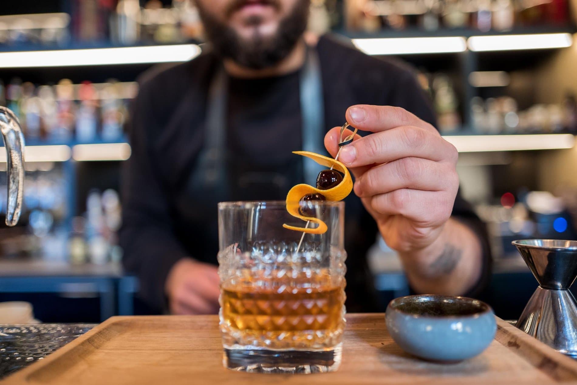 Bartender expertly garnishes an old-fashioned cocktail with orange twist at bar counter.