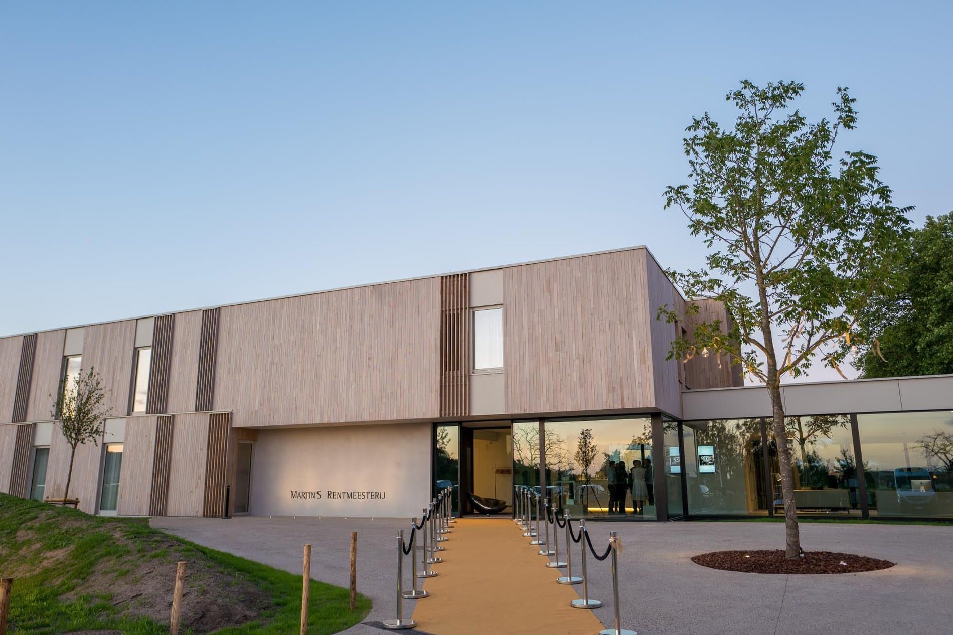 Modern wooden-clad hospitality building exterior with entrance ramp and welcoming grounds.