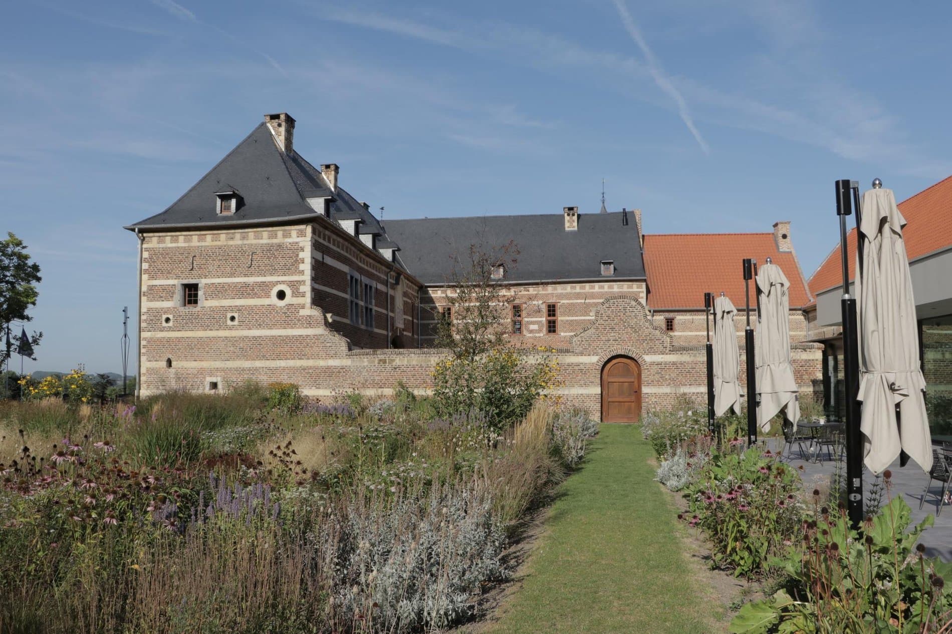 Historic stone mansion with manicured gardens and courtyard approach pathway.