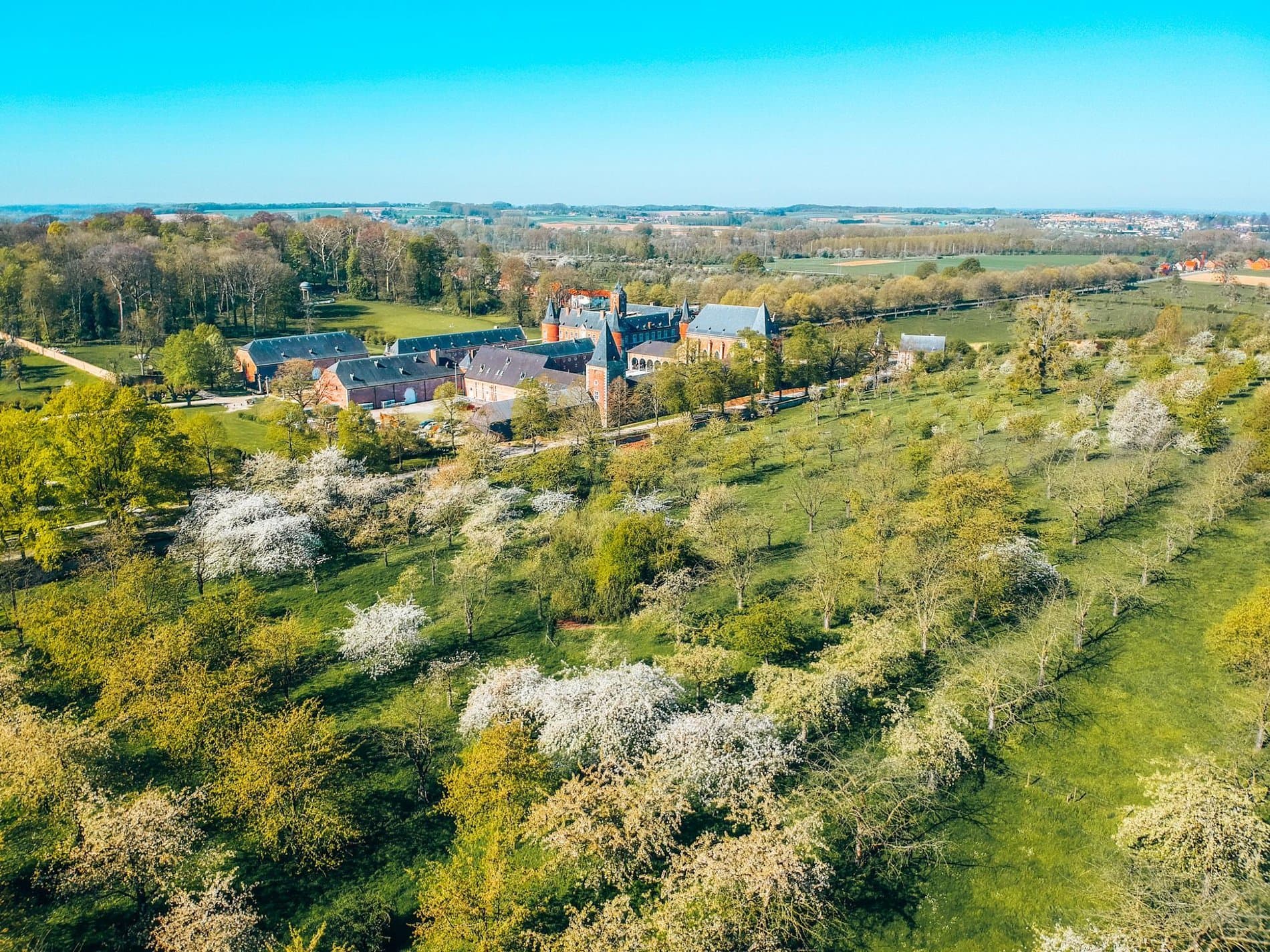 Historic brick estate with manicured gardens overlooks verdant countryside landscape.