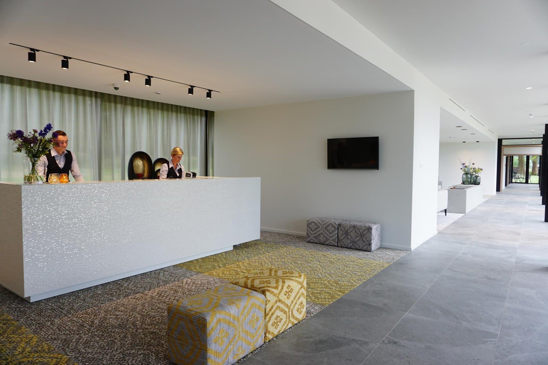 Modern hotel lobby with white reception desk, staff, and seating areas.