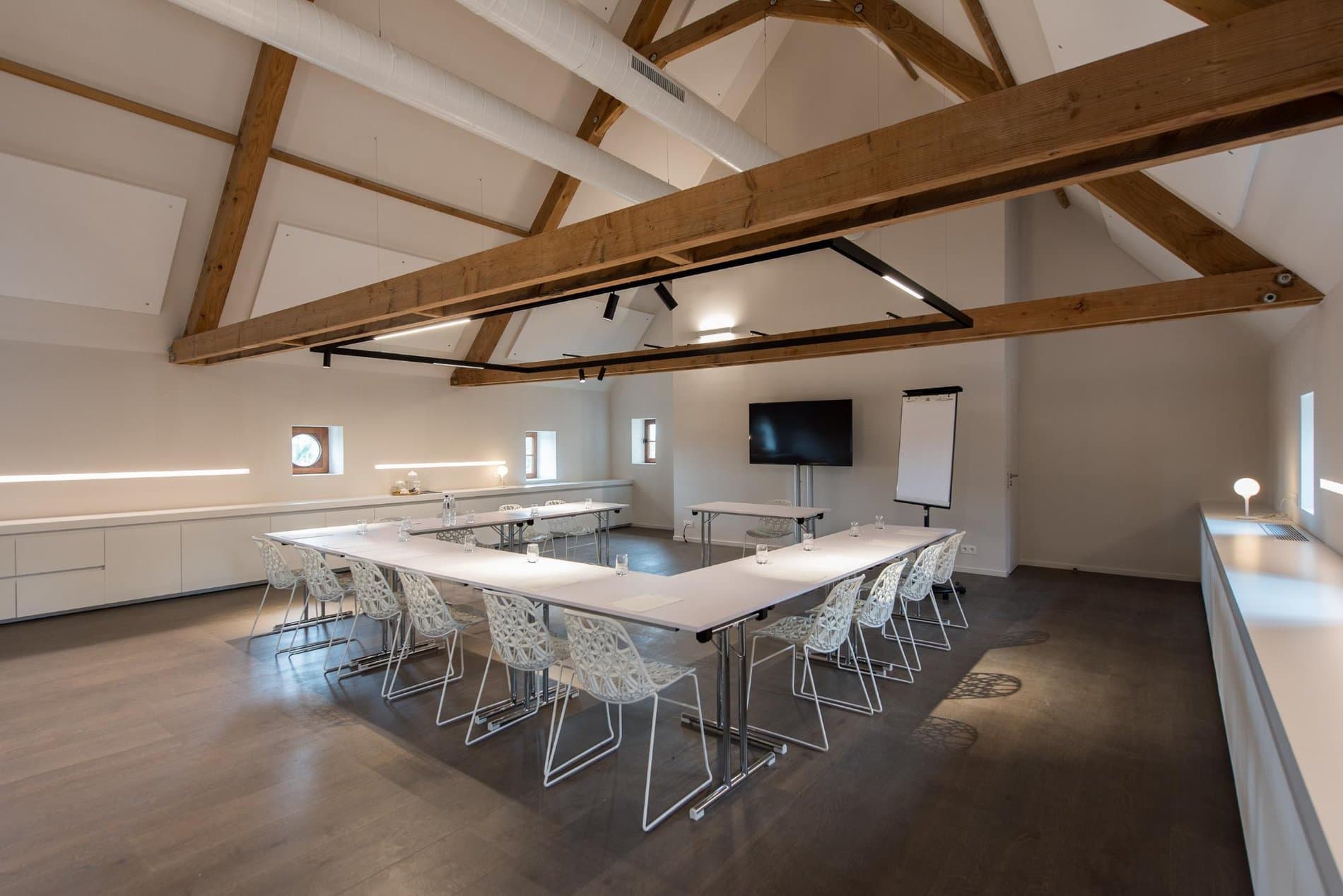 Modern conference room with exposed timber beams, U-shaped table setup, dining functionality.