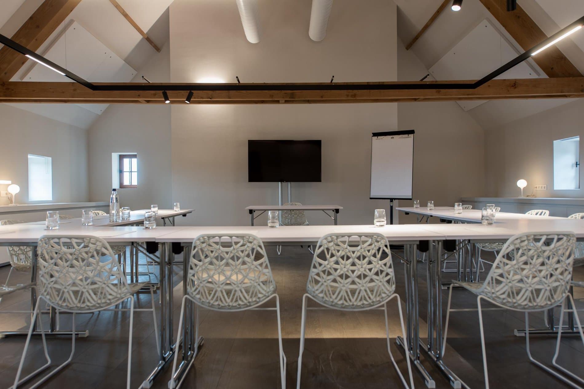 Modern meeting and dining space with long tables, modern chairs, and AV equipment setup.
