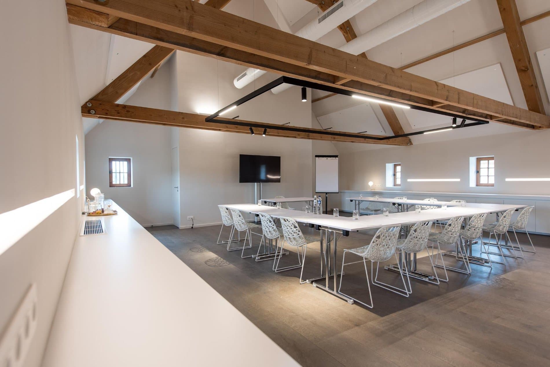 Modern conference room with vaulted wooden beams, dining setup, and presentation screen.