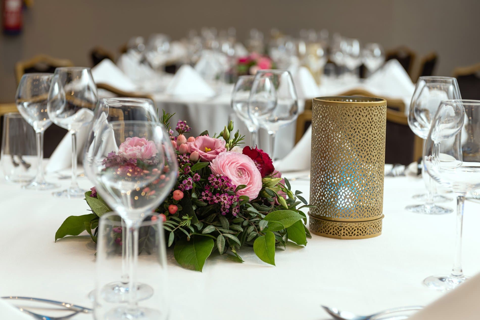 Elegant dining table setup with pink floral centerpiece, wine glasses, and gold candle holder.