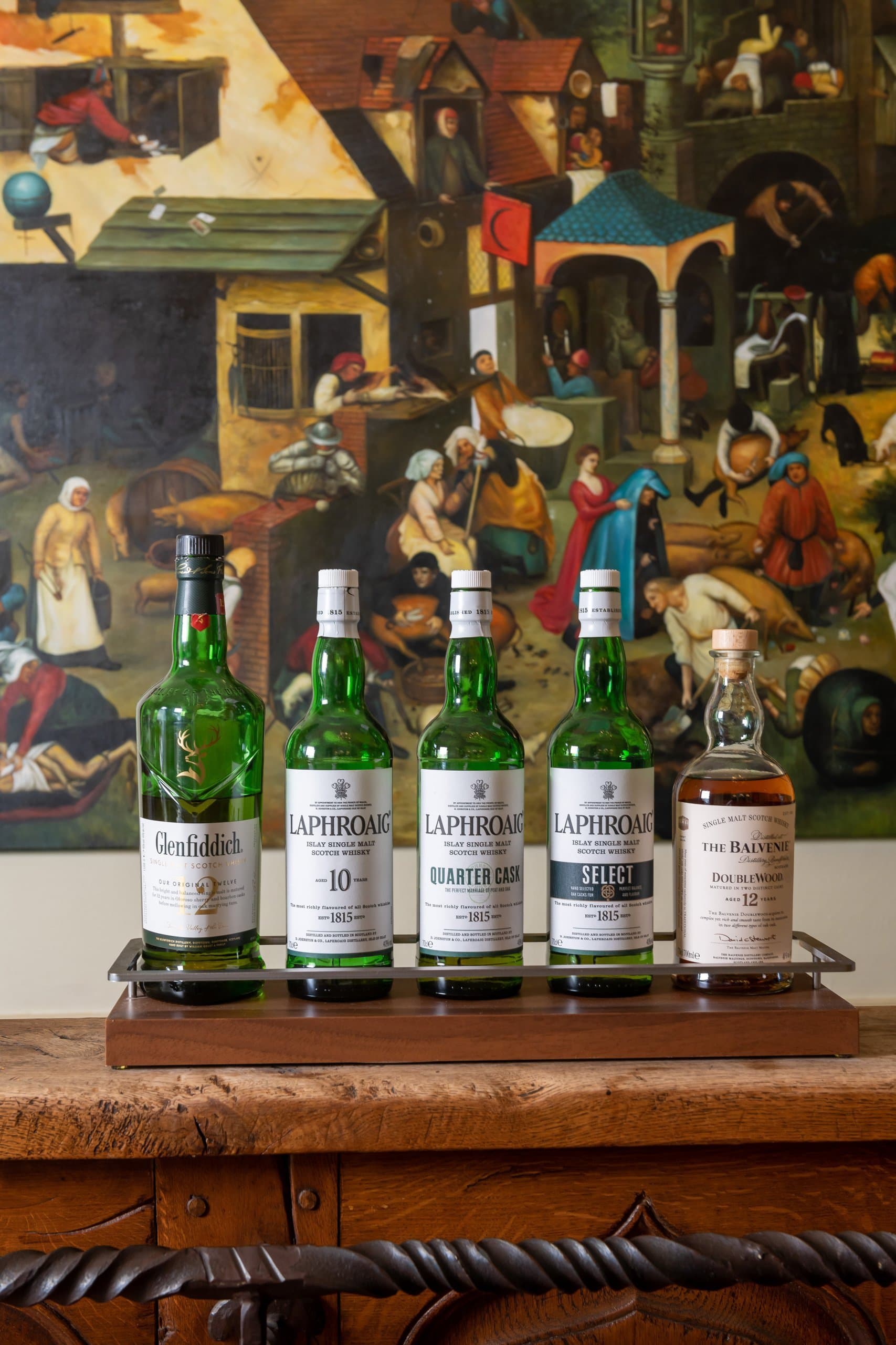 Collection of Scottish whisky bottles displayed against vintage tavern artwork backdrop.