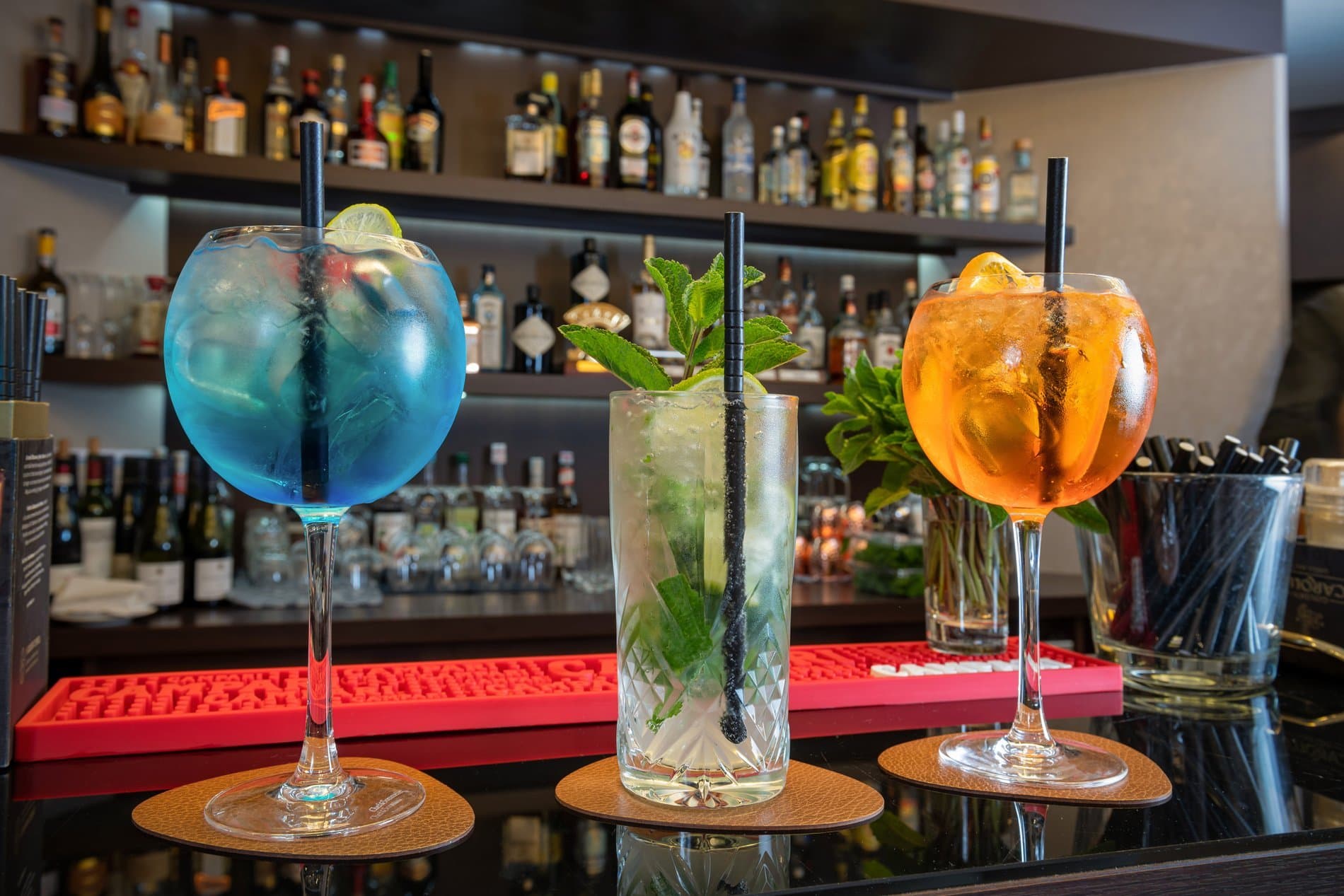 Professionally crafted cocktails displayed at bar with spirits bottles and wooden coasters.