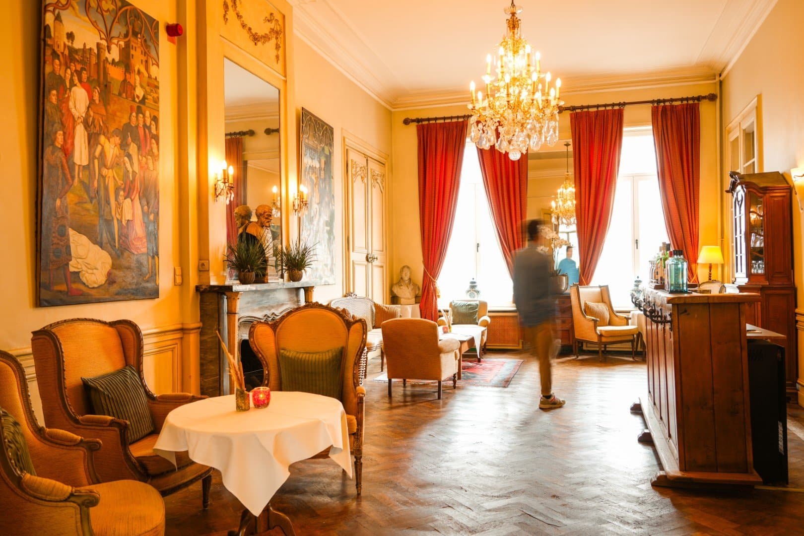 Elegant golden lounge with classical artwork, ornate chandelier, and plush seating areas.