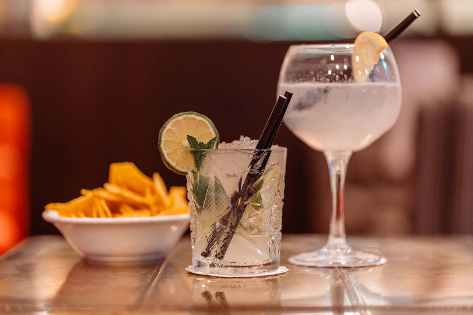 Refreshing cocktails with lime garnish, fries, and bar seating atmosphere displayed.