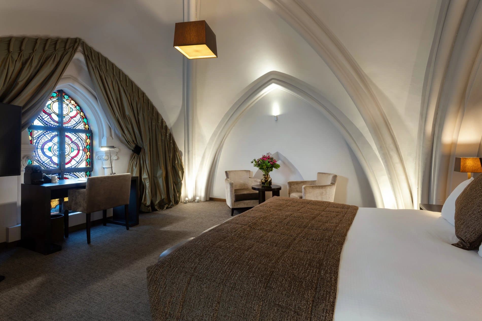 Luxury hotel suite with arched ceiling, stained glass window, and elegant furnishings.