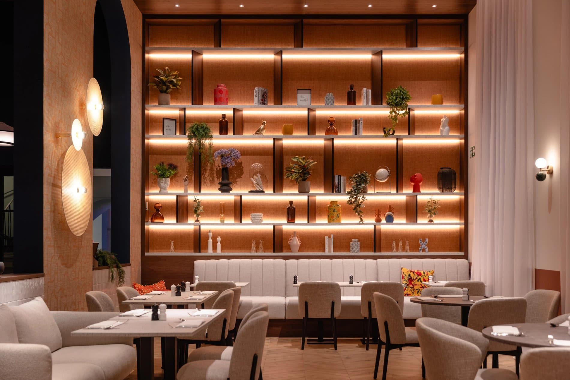 Modern restaurant dining area with illuminated shelving, tables, and contemporary decor throughout.