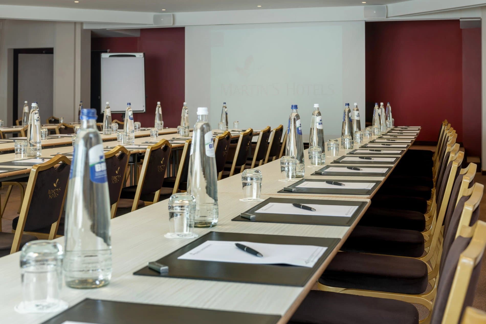 Large conference room with long tables, water bottles, notepads and comfortable seating arrangement.