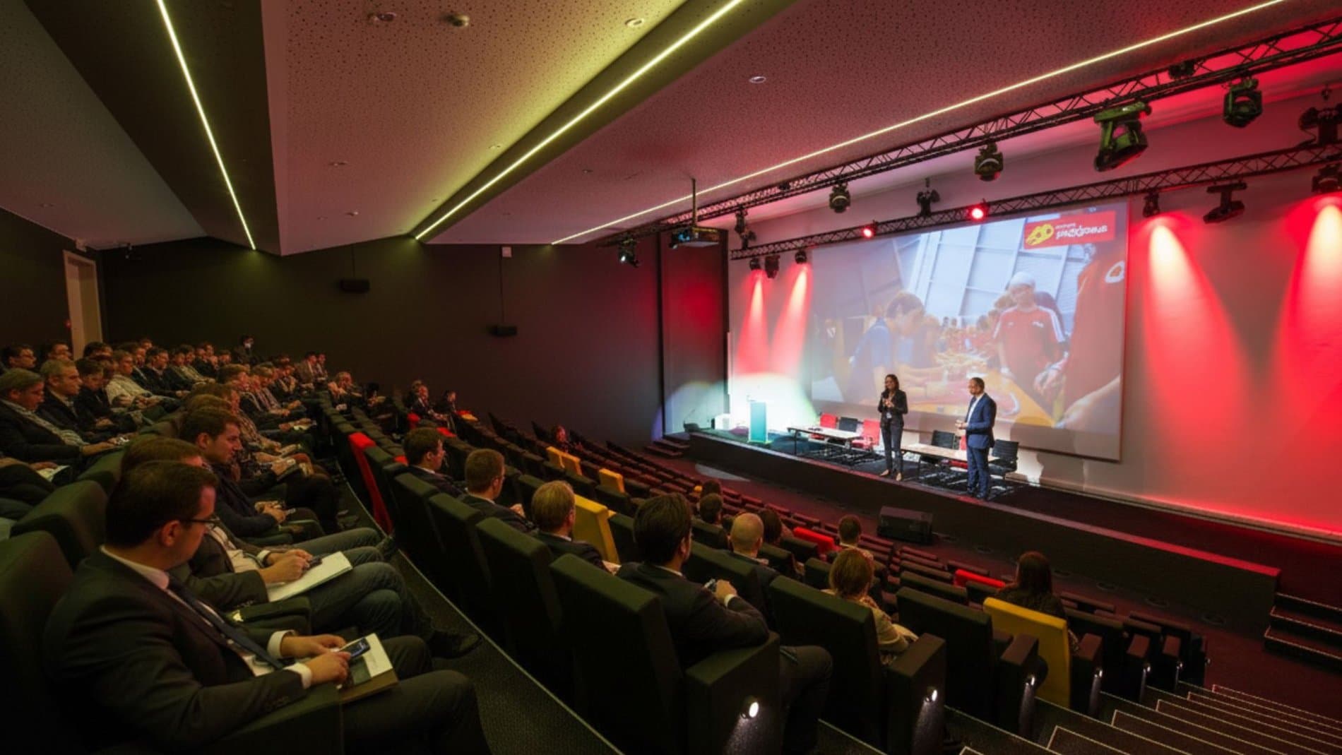 Modern conference room with theater seating, red ambient lighting, and projection screen.
