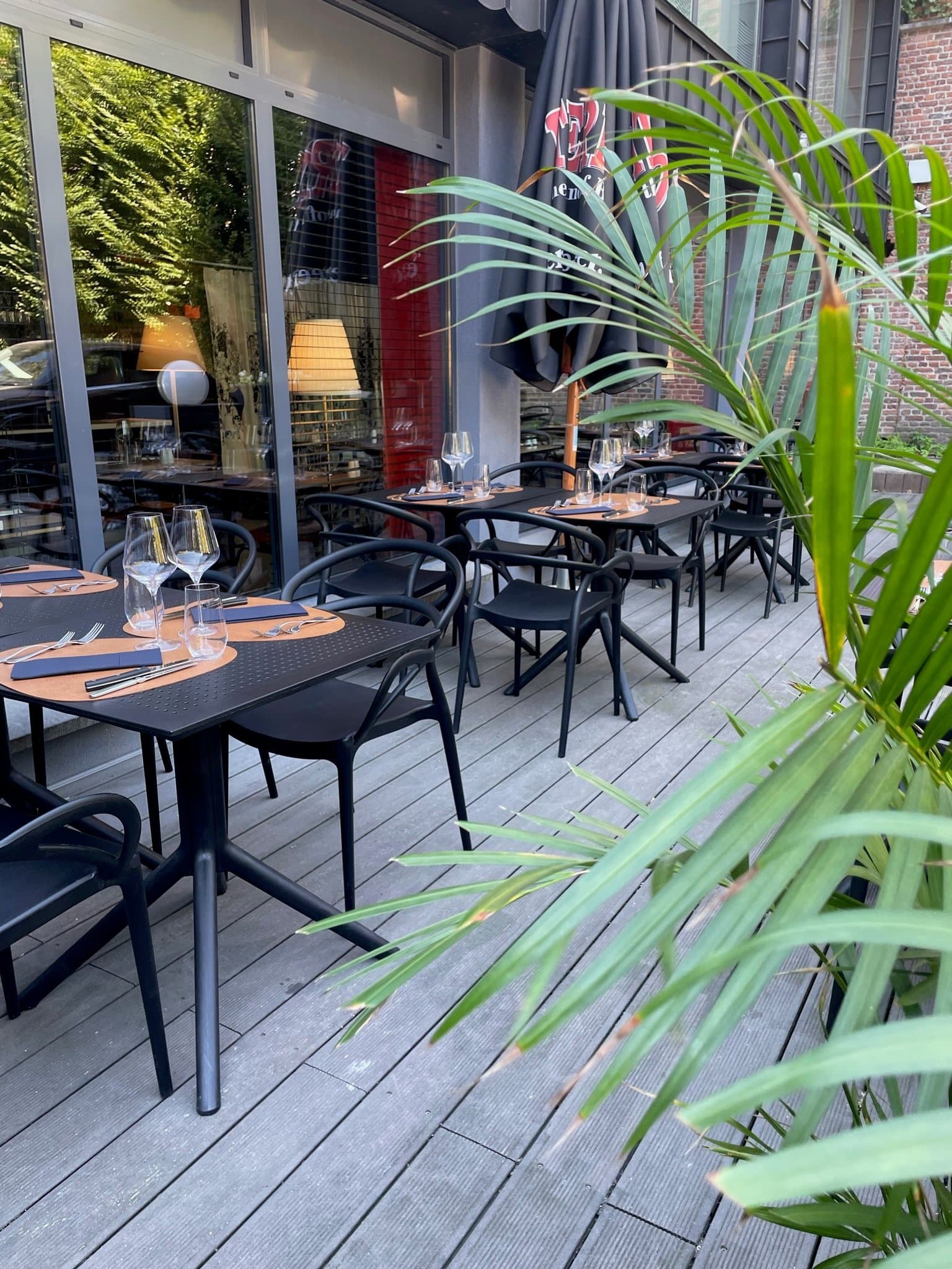 Restaurant terrace with black tables, chairs, place settings, and lush tropical plants.