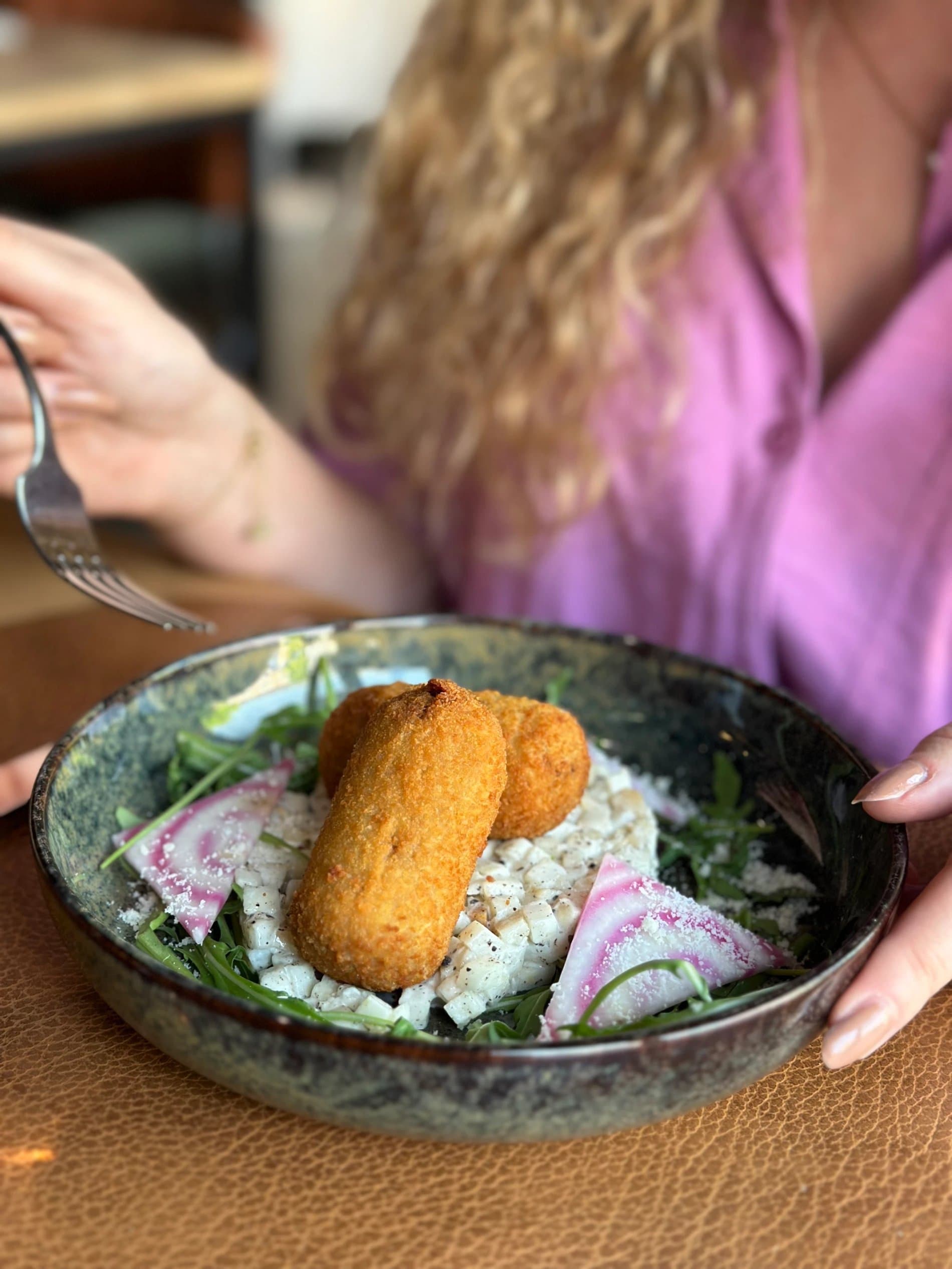 Gourmet plated dish with fried croquette, rice, greens, and purple pickled vegetables.