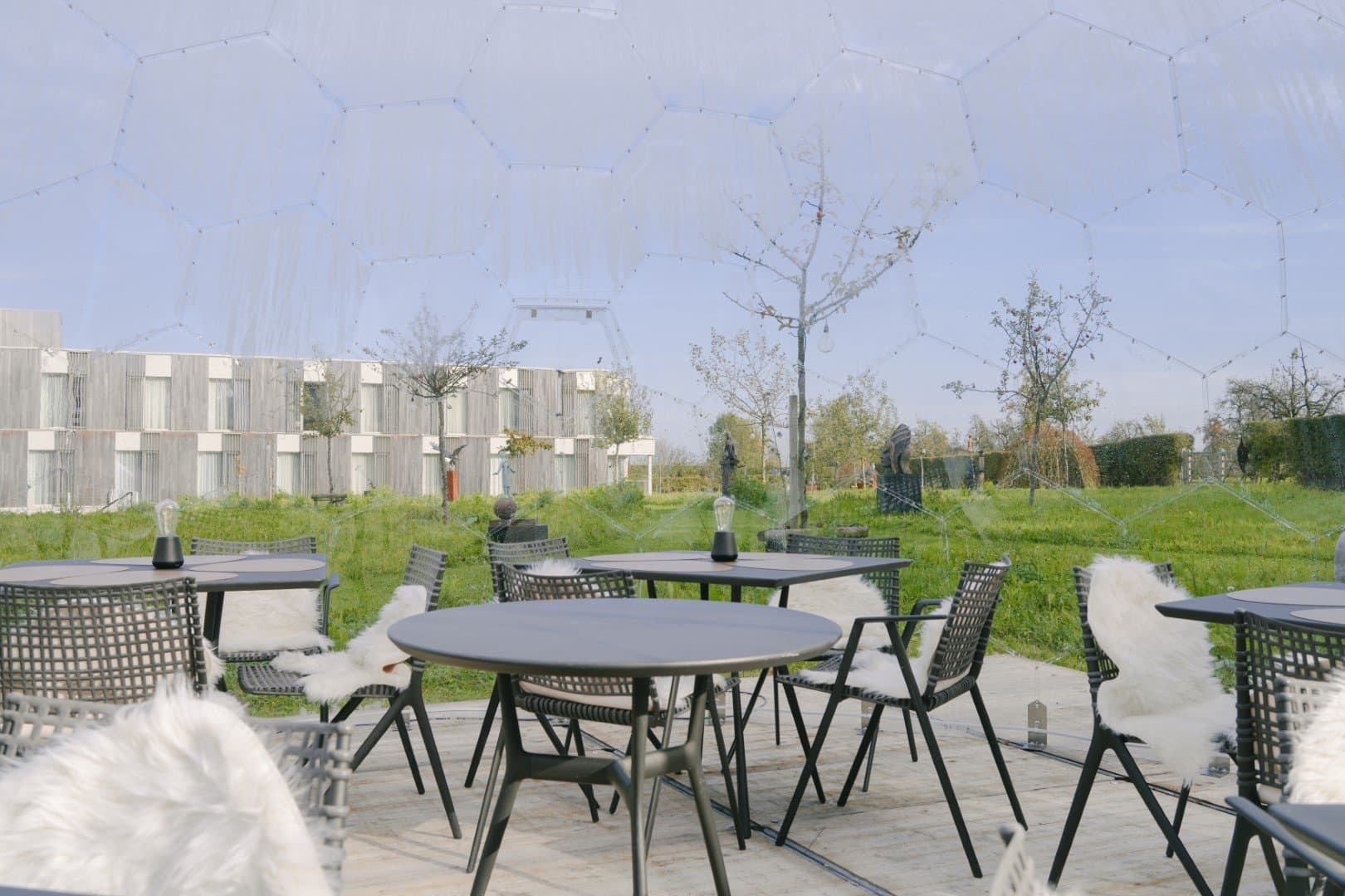 Modern outdoor terrace with contemporary furnishings and manicured green spaces surrounding building.